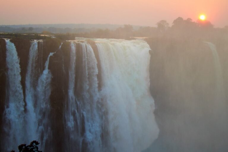 Victoria Falls in soft evening light with the sun setting behind the spray